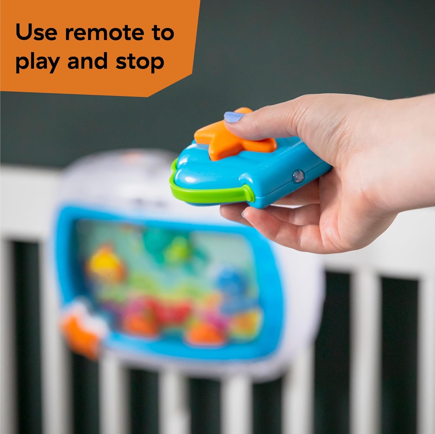 Hand using remote to control Baby Einstein crib soother, featuring colorful animal visuals.